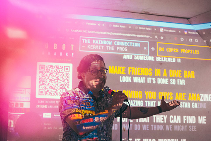 a man speaking into a microphone in front of a screen being projected with lyrics and graphics