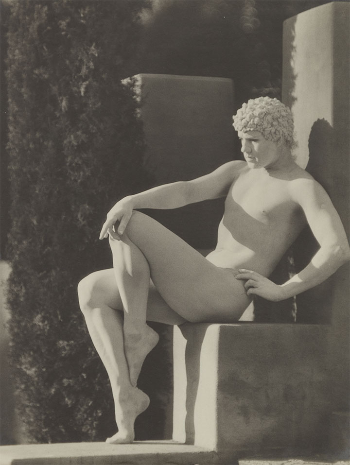 Black-and-white photograph of a man, statuelike and all white, posting on a block of cement.