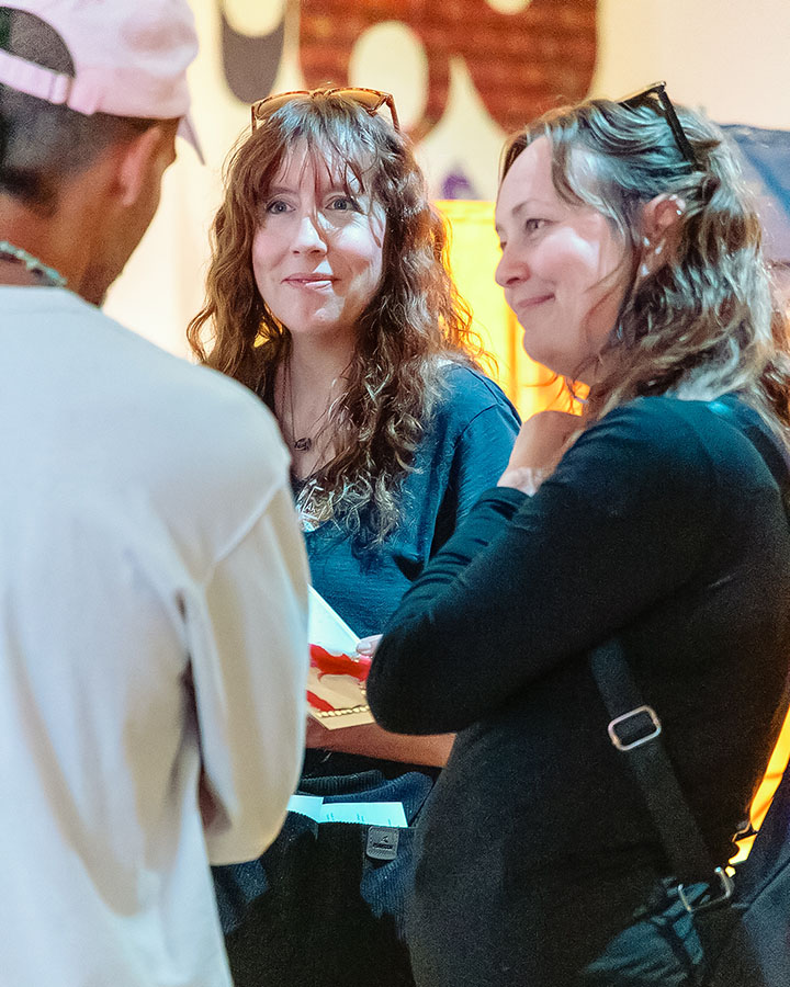 Two women sharing a delightful conversation in the galleries with a friend in a pink baseball cap.
