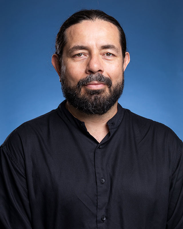 Portrait of a bearded man wearing a black shirt against a blue background
