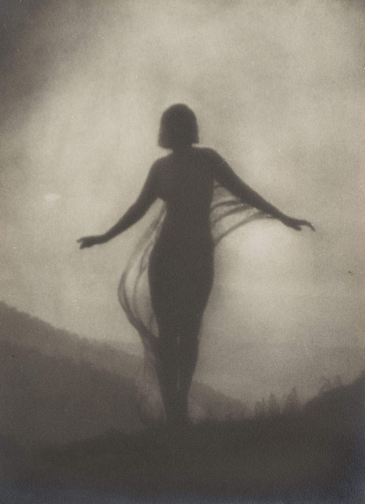 black and white photo featuring a silhouette of a figure, presumably a woman, with their arms raised slightly standing outdoors