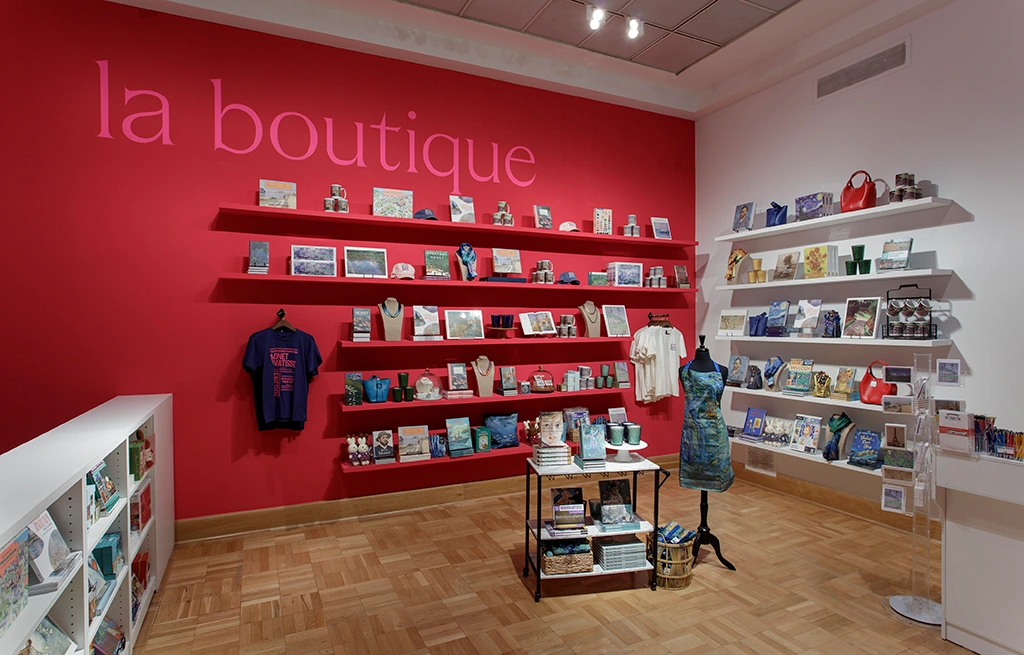 photo of pop-up store in galley featuring art themed merchandise along the back wall, painted magenta, including books, shirts, puzzles and more
