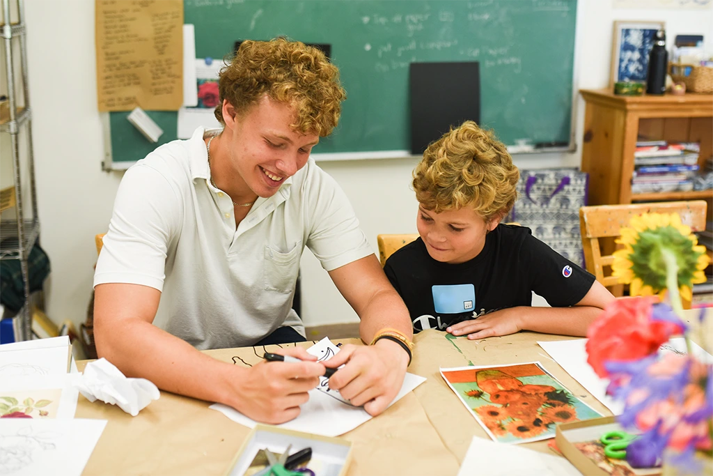 smiling teenager working with young boy at a crafting table